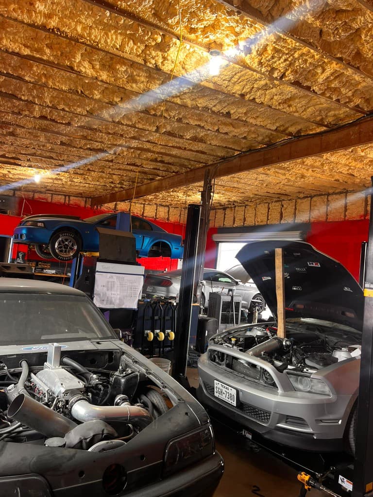 Mustangs and a Camaro on lifts inside the shop